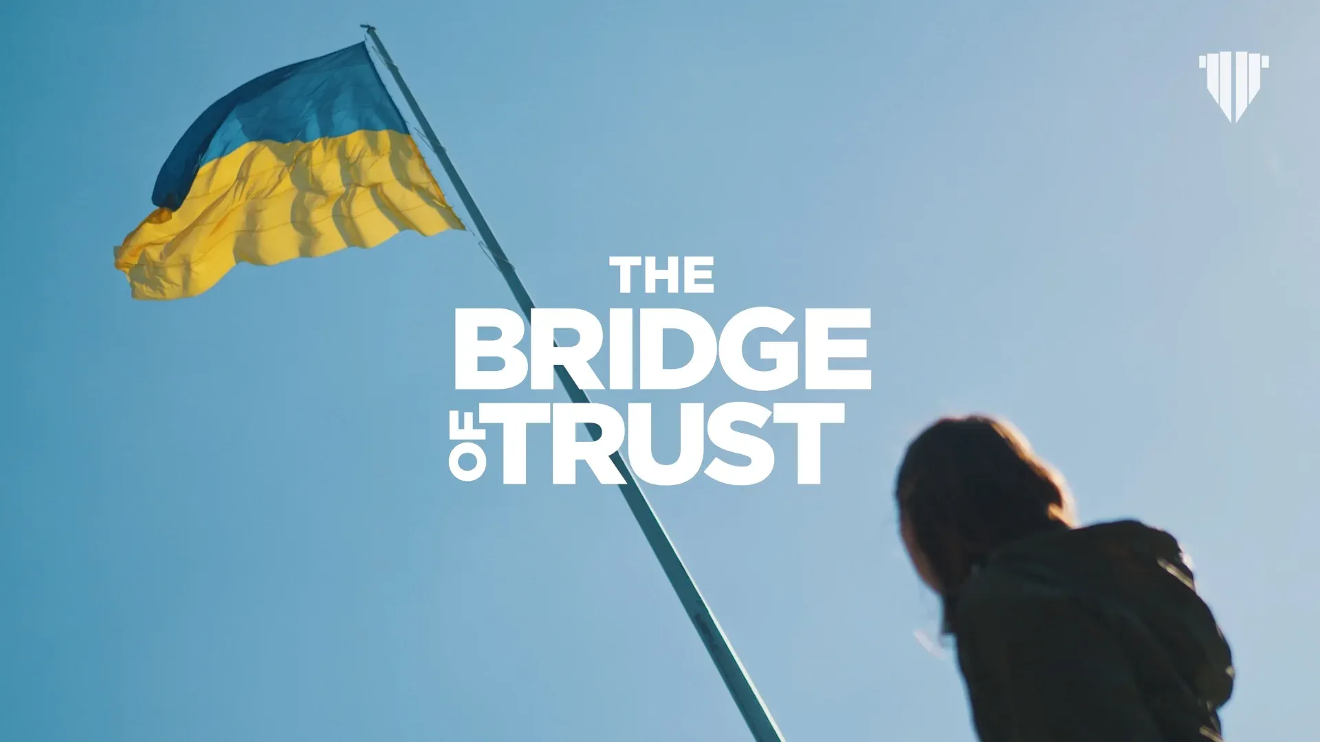 The Bridge of Trust logo against a blue sky, with a Ukrainian flag and a person looking up.